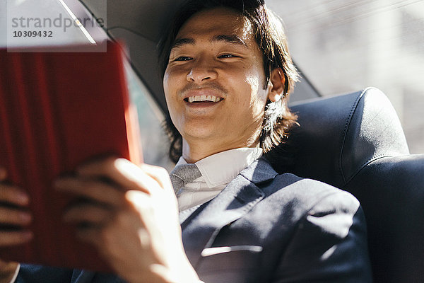 Lächelnder Geschäftsmann auf dem Rücksitz eines Autos mit digitalem Tablett