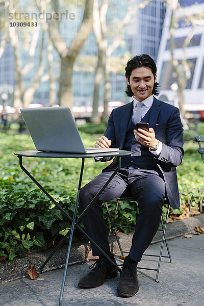 USA  New York City  Manhattan  lächelnder Geschäftsmann mit Laptop und Handy in Bryant Park