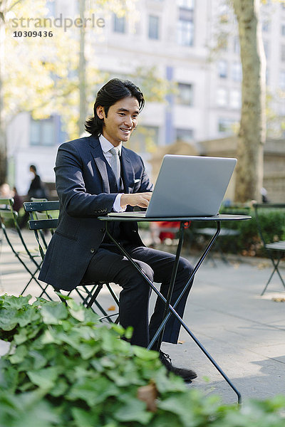 USA  New York City  Manhattan  lächelnder Geschäftsmann bei der Arbeit mit einem Laptop im Bryant Park