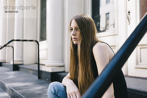 USA  New York City  nachdenkliche junge Frau auf einer Treppe vor einer Eingangstür sitzend