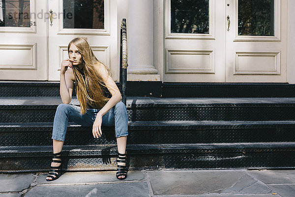 USA  New York City  nachdenkliche junge Frau auf einer Treppe vor einer Eingangstür sitzend