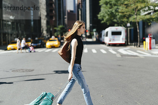 USA  New York City  junge Frau mit Rollkoffer überquert eine Straße
