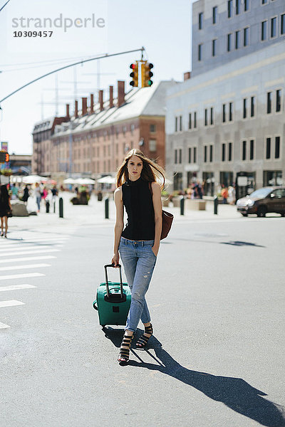 USA  New York City  junge Frau mit Rollkoffer auf einer Straße stehend