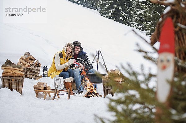 Lächelndes Paar im Schnee am Lagerfeuer