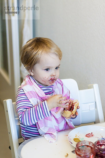 Kleines Mädchen mit Lätzchen versucht  Marmeladenbrötchen zu essen.