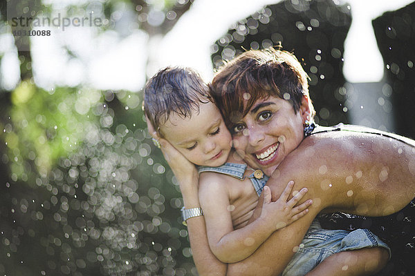 Lttle Boy und seine Mutter genießen das spritzende Wasser im Garten.