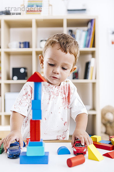 Porträt eines aufgeregten kleinen Jungen  der mit Bausteinen und Spielzeugautos spielt.