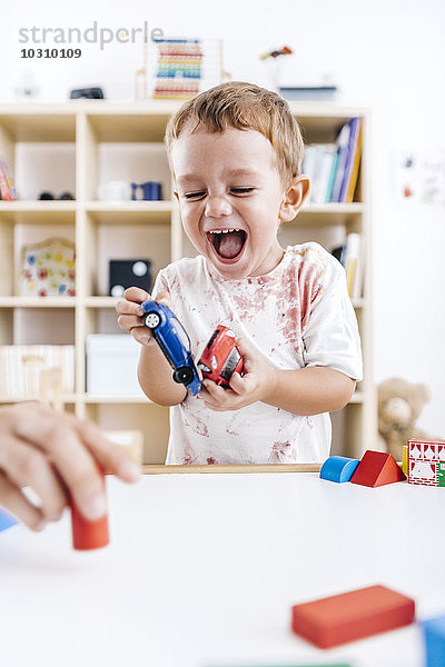Porträt des lachenden kleinen Jungen beim Spielen mit Spielzeugautos