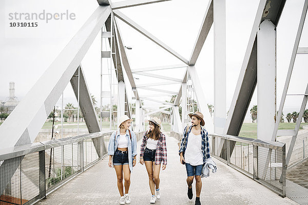 Spanien  Barcelona  drei glückliche Freunde  die Seite an Seite auf einer Brücke gehen.