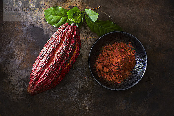 Kakaoschote und Schale mit Kakao auf rostigem Grund