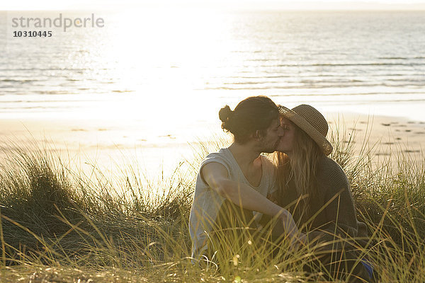Junges Paar beim Küssen an den Stranddünen vor dem Atlantik