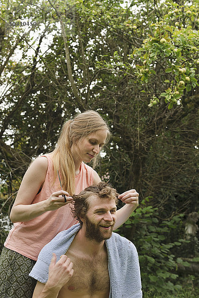 Junge Frau schneidet Haare von ihrem Freund im Garten