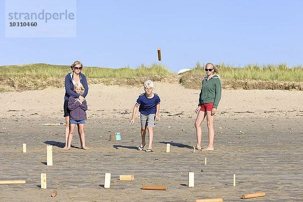 Mutter und drei Kinder spielen Kubb am Strand