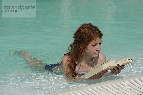 Rothaariges Mädchen liegt im Schwimmbad und liest ein Buch.