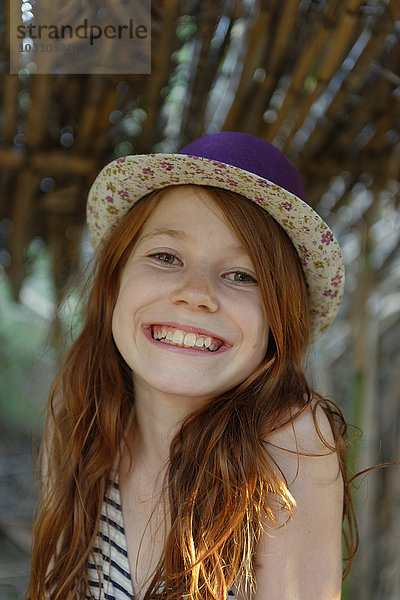 Porträt des grinsenden rothaarigen Mädchens mit Hut