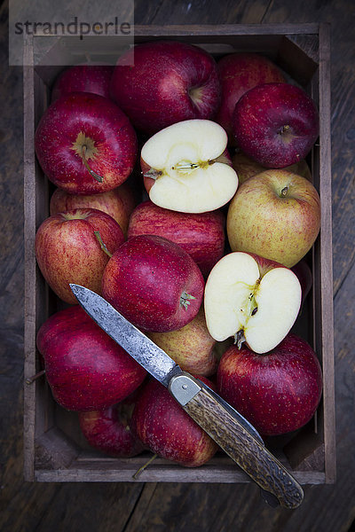 Holzkiste mit roten Äpfeln und Taschenmesser