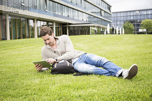 Deutschland  Tübingen  junger Mann entspannt auf einer Wiese mit digitalem Tablett