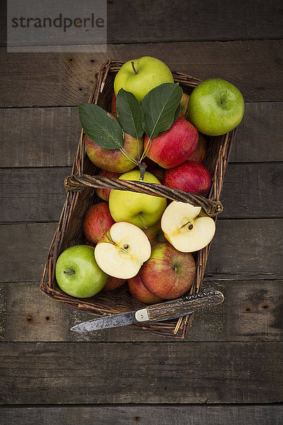 Verschiedene Äpfel  Korb und Taschenmesser auf Holz