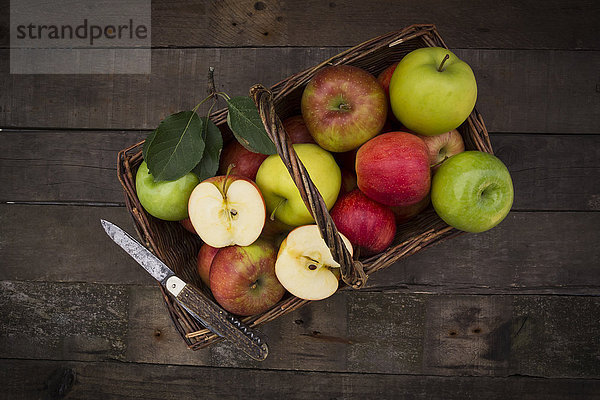 Verschiedene Äpfel  Korb und Taschenmesser auf Holz