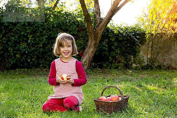 Porträt eines lächelnden kleinen Mädchens auf einer Wiese mit Apfelkorb