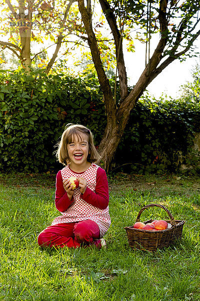 Porträt eines lachenden kleinen Mädchens auf einer Wiese mit Apfelkorb