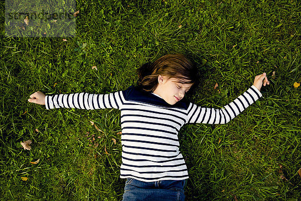 Mädchen in gestreiftem Sweatshirt auf einer Wiese liegend mit geschlossenen Augen