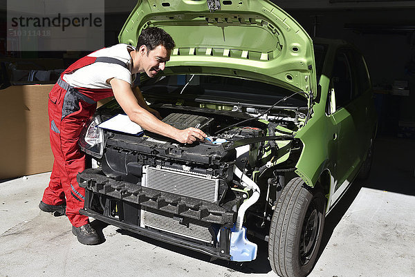 Kfz-Mechaniker untersucht unfallbeschädigtes Auto vor der Reparatur
