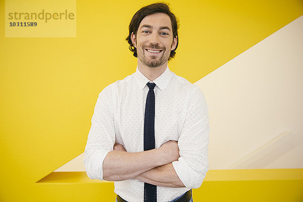 Portrait eines reifen Mannes mit Hemd und Krawatte vor einer gelben Wand stehend