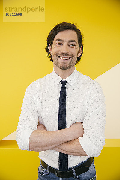 Porträt eines lächelnden reifen Mannes mit Hemd und Krawatte vor einer gelben Wand stehend