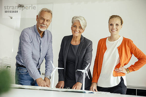 Drei lächelnde Geschäftsleute mit Windkraftanlagenmodell auf dem Konferenztisch