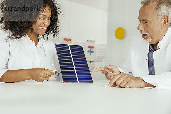 Zwei Wissenschaftler im Gespräch über ein Solarpanel mit Voltmeter im Labor
