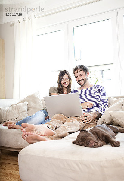 Lächelndes Paar entspannt mit Laptop auf der Couch im Wohnzimmer