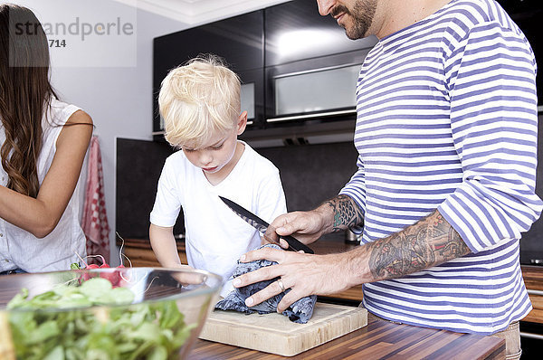 Mann hackt Rotkohl in der Küche  während sein Sohn zusieht.