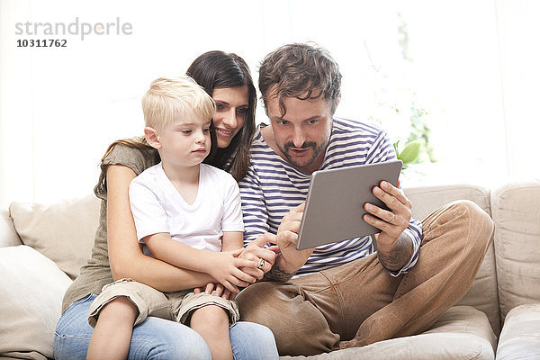 Eltern und kleiner Sohn sitzen auf der Couch mit digitalem Tablett