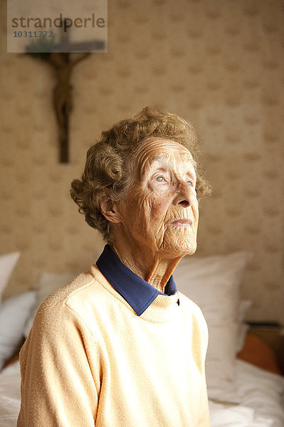 Porträt einer alten Frau  die in ihrem Schlafzimmer auf dem Bett sitzt.