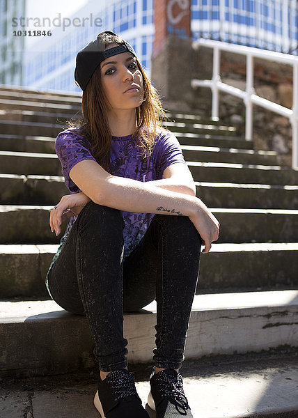 Porträt einer jungen Frau mit Baseballmütze auf einer Treppe sitzend