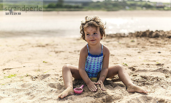 Porträt eines lächelnden kleinen Mädchens im Badeanzug beim Spielen am Strand