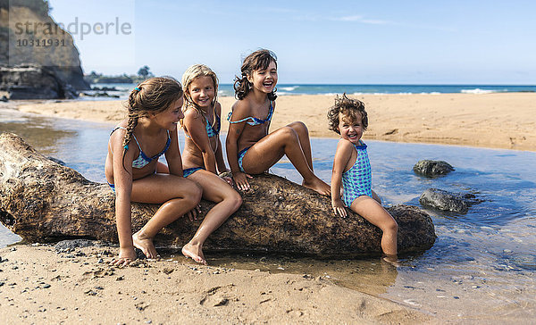 Spanien  Colunga  vier Mädchen auf Totholz am Strand sitzend