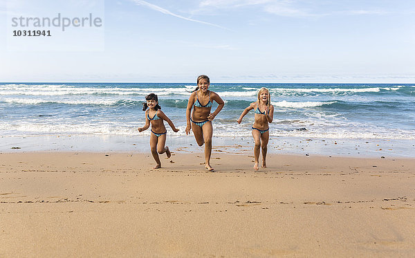 Spanien  Colunga  drei Mädchen  die Seite an Seite am Strand laufen.