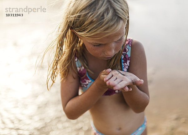 Kleines Mädchen am Strand mit einem Aal an der Hand