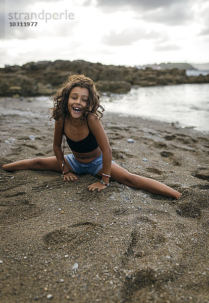 Spanien  Gijon  Porträt eines lächelnden kleinen Mädchens  das die Spaltung am Strand macht
