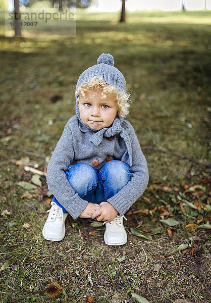 Porträt eines kleinen Jungen  der auf einer Wiese hockt.