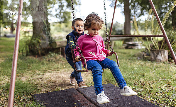 Zwei kleine Kinder spielen mit Schaukel im Garten