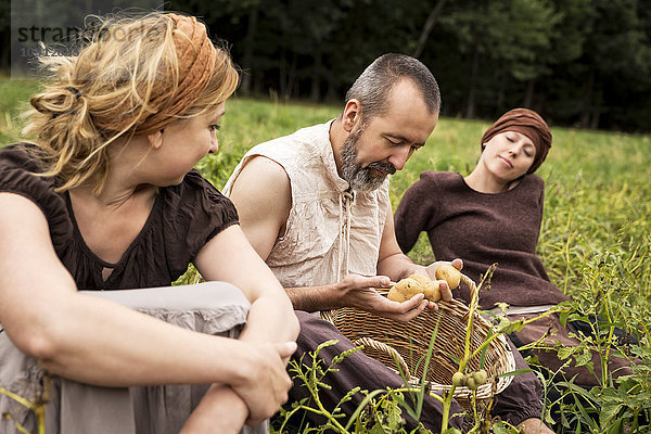 Drei Personen sitzen auf dem Feld mit Kartoffeln im Weidenkorb