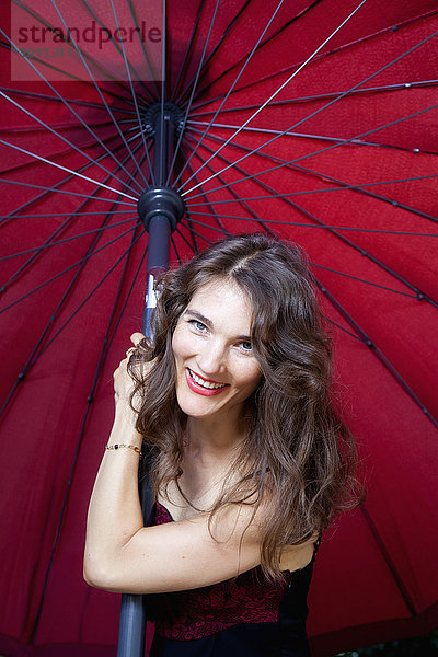 Porträt der lächelnden Frau vor dunkelrotem Sonnenschirm