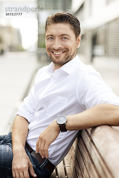 Porträt eines lächelnden Mannes in weißem Hemd auf Holzbank sitzend