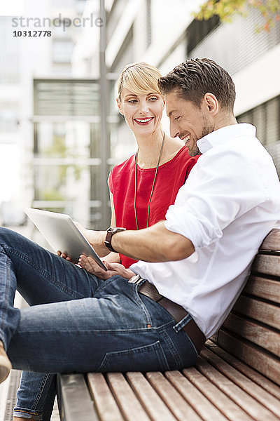 Paar sitzend nebeneinander auf Holzbank mit digitalem Tablett