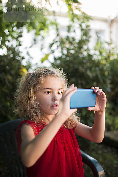 Kleines Mädchen in rotem Kleid fotografiert mit Smartphone