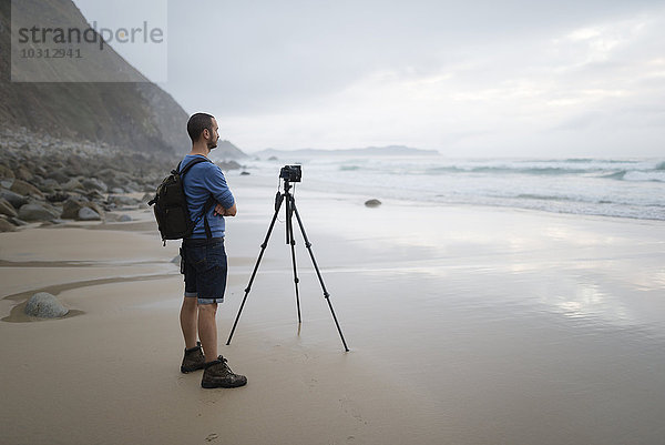 Spanien  Valdovino  Fotograf steht am Strand und fotografiert mit einem Stativ.