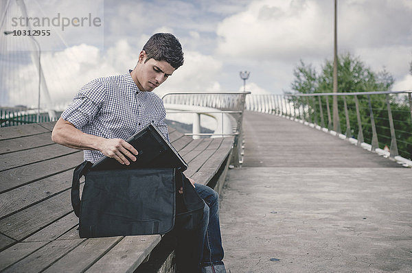 Spanien  Ferrol  junger Mann nimmt seinen Laptop aus der Tasche